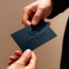 Hand holding a dark blue business card with 'Leonidas Securite' logo against a beige background